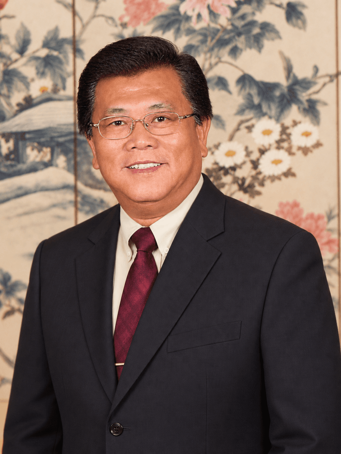 Robert smiling in a dark suit in front of a floral screen